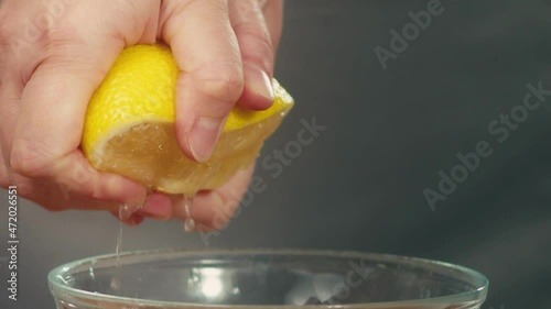 Woman uses hands to squeeze out half of ripe yellow lemon juice with drops dripping down into transparent bowl macro slow motion