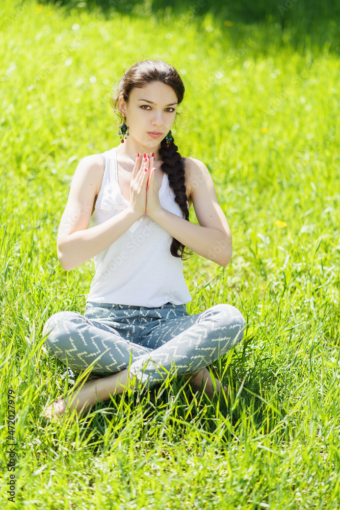 Young woman sitting in a lotus position on a green lawn. Soft focus on eyes. Young woman sitting in a lotus position on a green lawn. Soft focus on eyes.