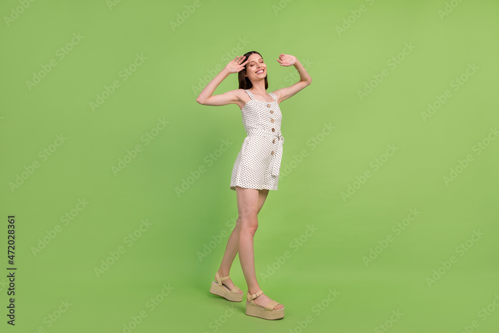 Full length photo of funny young brunette lady go wear overall sandals isolated on green background Full length photo of funny young brunette lady go wear overall sandals isolated on green background