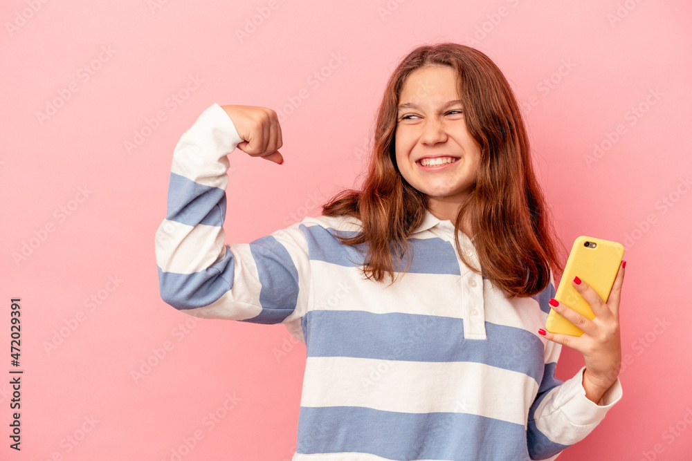 Little caucasian girl holding mobile phone isolated on pink background raising fist after a victory, winner concept.