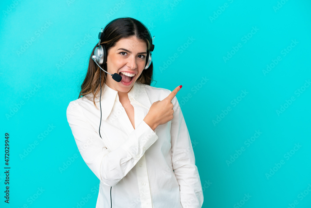 Telemarketer Italian woman working with a headset isolated on blue background surprised and pointing side Telemarketer Italian woman working with a headset isolated on blue background surprised and pointing side