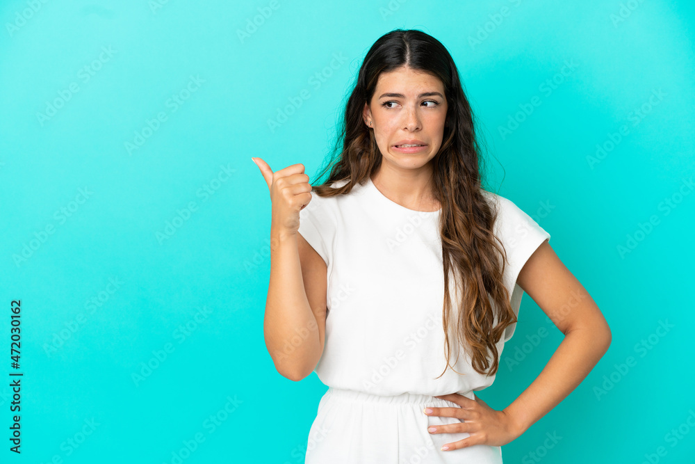Fototapeta premium Young caucasian woman isolated on blue background unhappy and pointing to the side