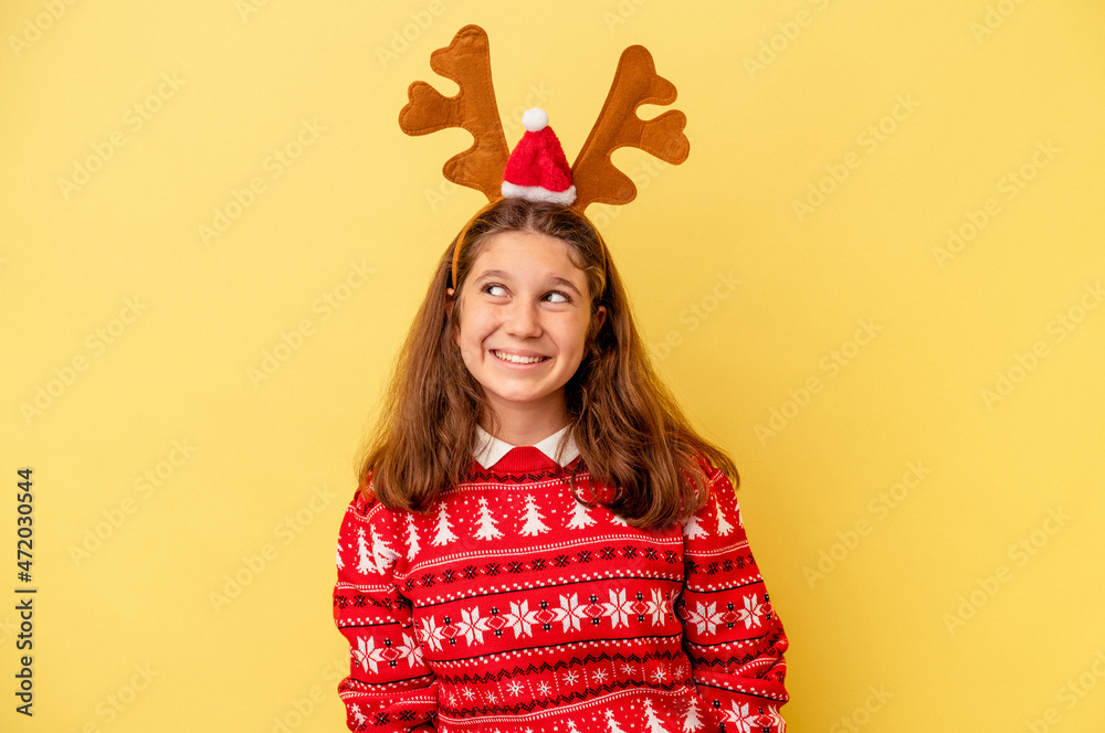 Little caucasian girl wearing a Christmas reindeer hat isolated on yellow background dreaming of achieving goals and purposes Little caucasian girl wearing a Christmas reindeer hat isolated on yellow background dreaming of achieving goals and purposes
