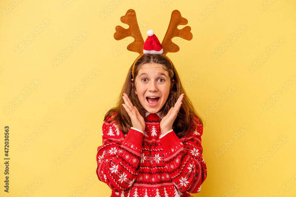 Little caucasian girl wearing a Christmas reindeer hat isolated on yellow background surprised and shocked. Little caucasian girl wearing a Christmas reindeer hat isolated on yellow background surprised and shocked.