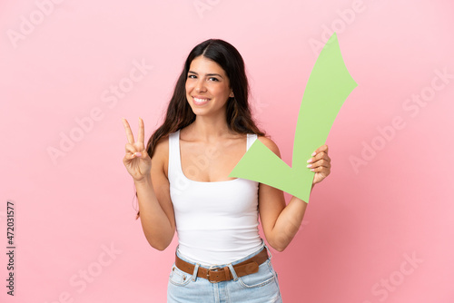 Young caucasian woman isolated on pink background holding a check icon and celebrating a victory