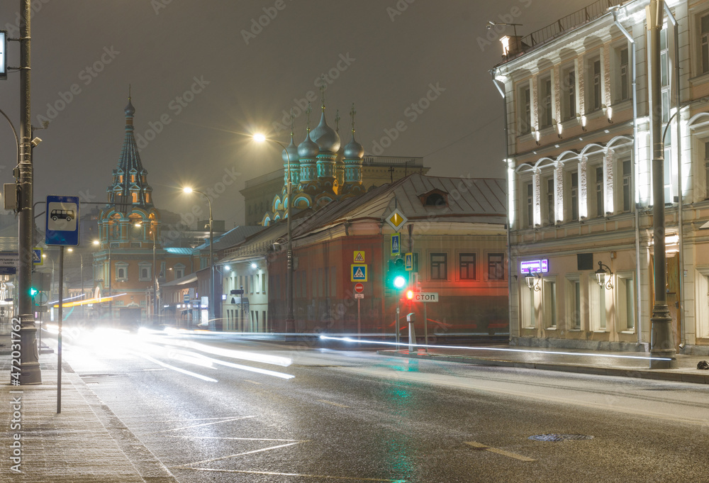 Moscow, Russia, Nov 19, 2021: Night view of Bolshaya Polyanka street. Church of st. Gregory of Neocaesarea. Beginning of snowfall. Car traces