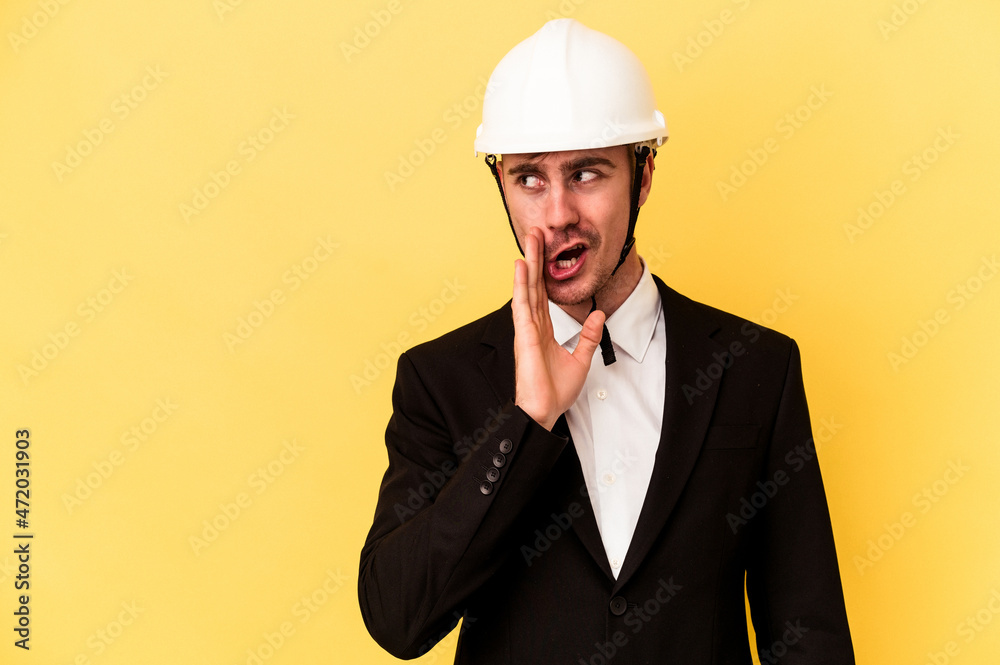 Young architect caucasian man isolated on yellow background is saying a secret hot braking news and looking aside Young architect caucasian man isolated on yellow background is saying a secret hot braking news and looking aside