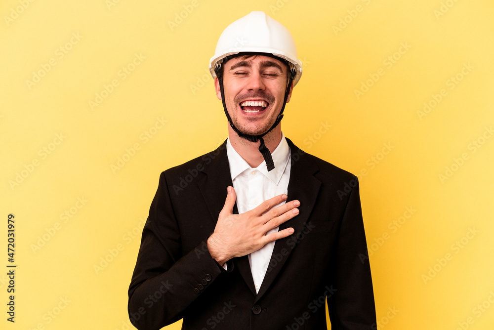 Young architect caucasian man isolated on yellow background laughs out loudly keeping hand on chest. Young architect caucasian man isolated on yellow background laughs out loudly keeping hand on chest.