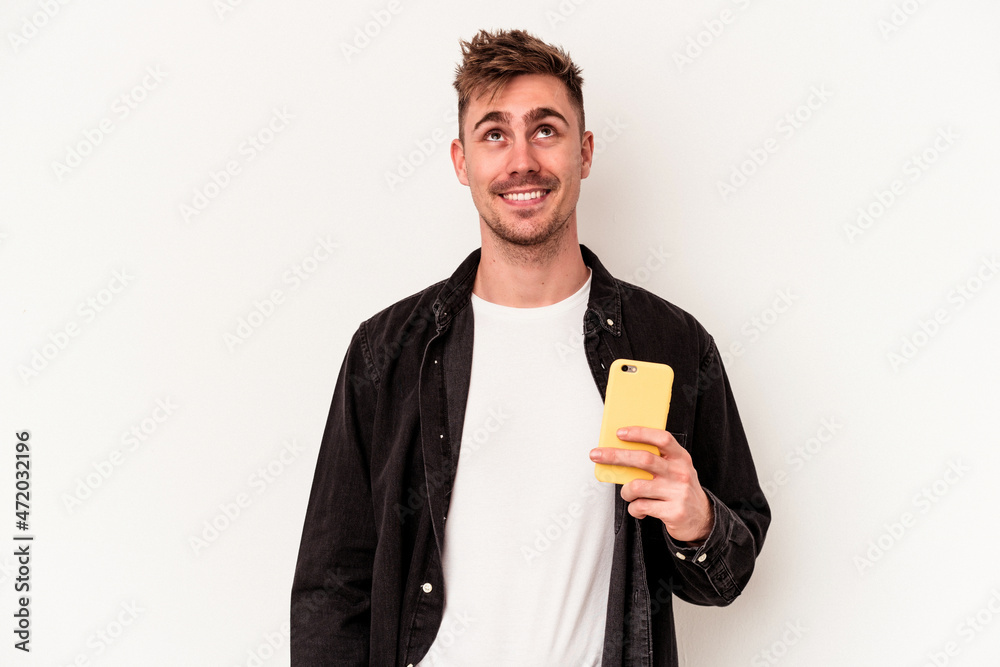 Young caucasian man holding a mobile phone isolated on white background dreaming of achieving goals and purposes Young caucasian man holding a mobile phone isolated on white background dreaming of achieving goals and purposes