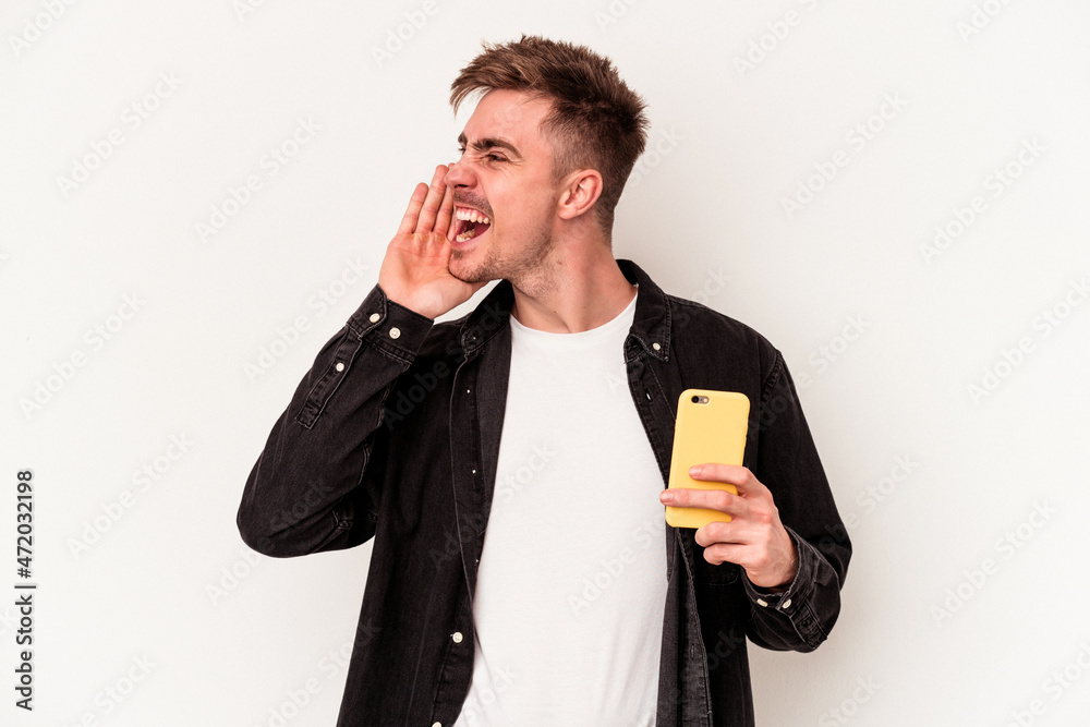 Young caucasian man holding a mobile phone isolated on white background shouting and holding palm near opened mouth. Young caucasian man holding a mobile phone isolated on white background shouting and holding palm near opened mouth.