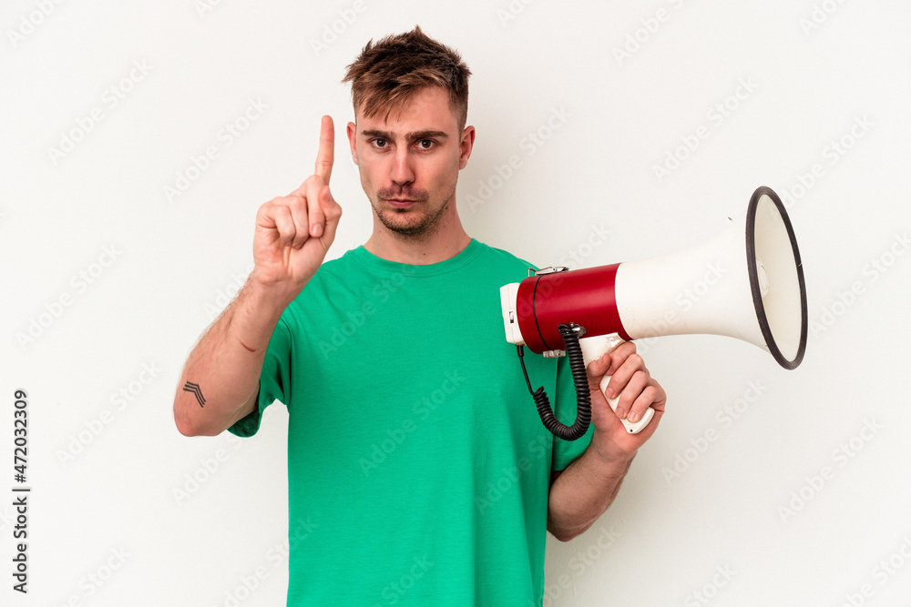 Young caucasian man holding megaphone isolated on white background showing number one with finger. Young caucasian man holding megaphone isolated on white background showing number one with finger.
