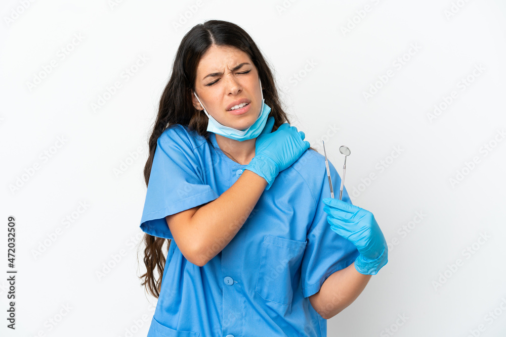 Dentist woman holding tools over isolated white background suffering from pain in shoulder for having made an effort Dentist woman holding tools over isolated white background suffering from pain in shoulder for having made an effort