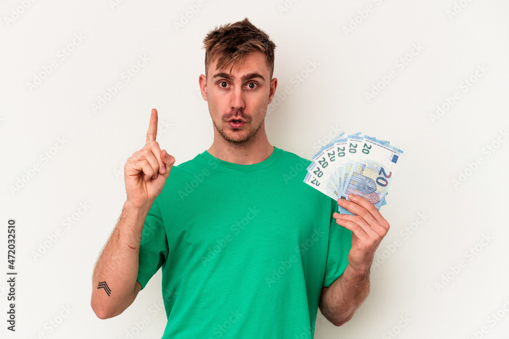 Young caucasian man holding bank notes isolated on white background having some great idea, concept of creativity. Young caucasian man holding bank notes isolated on white background having some great idea, concept of creativity.