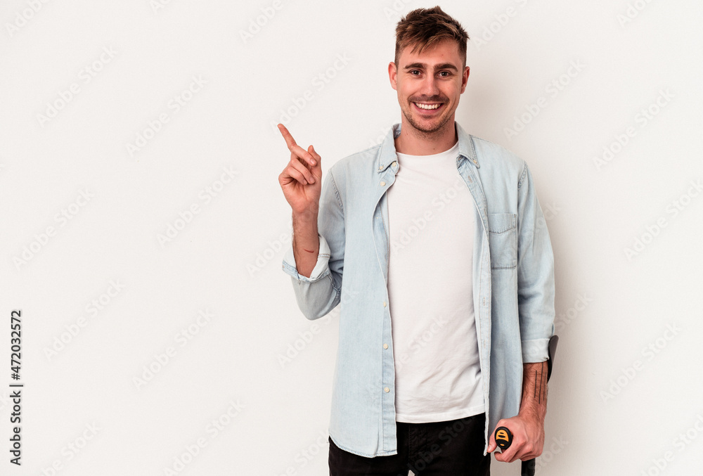 Young caucasian man holding crutch isolated on white background smiling and pointing aside, showing something at blank space. Young caucasian man holding crutch isolated on white background smiling and pointing aside, showing something at blank space.