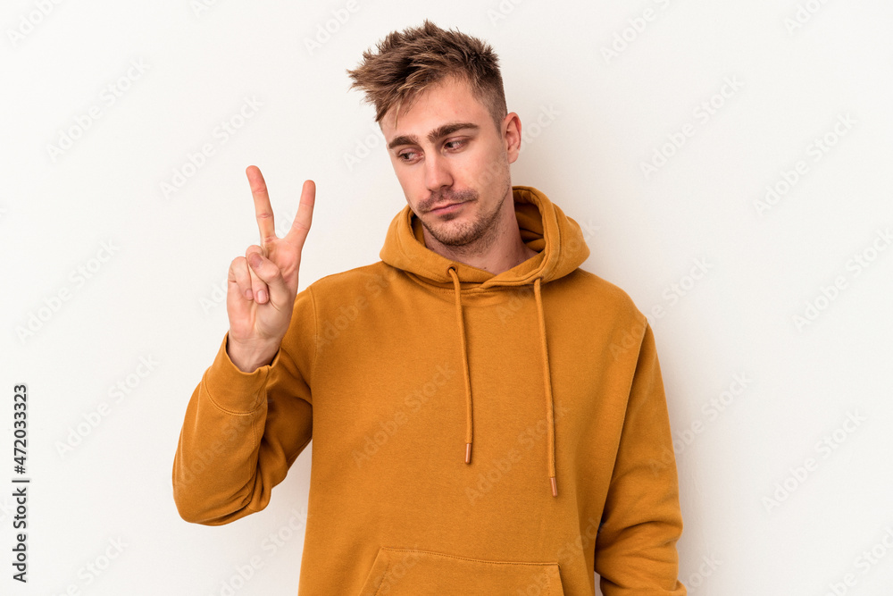Young caucasian man isolated on white background joyful and carefree showing a peace symbol with fingers.