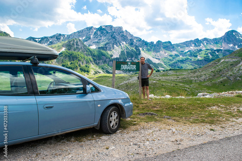 Man tourist near sign with the inscription Durmitor and car on background mountains Durmitor National Park. Montenegro.