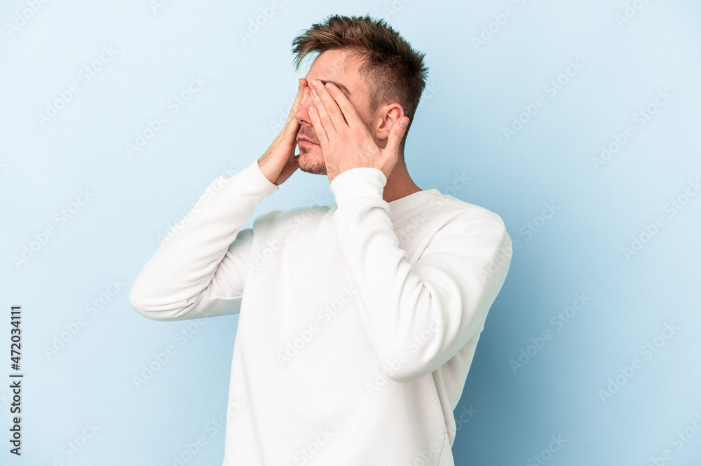 Young caucasian man isolated on blue background afraid covering eyes with hands. Young caucasian man isolated on blue background afraid covering eyes with hands.