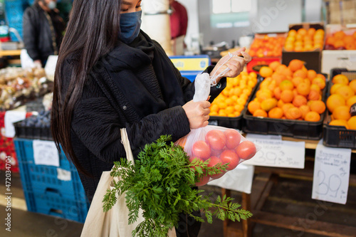 A woman at a farmer's market holds a cotton grocery eco-bag with vegetables and fruits. The concept of zero waste, no plastic, eco-friendly shopping, healthy lifestyle and proper nutrition
