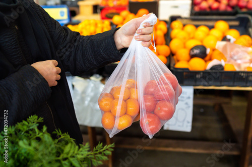 A woman at a farmer's market holds a cotton grocery eco-bag with vegetables and fruits. The concept of zero waste, no plastic, eco-friendly shopping, healthy lifestyle and proper nutrition