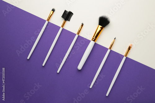 Various makeup brushes on purple and grey background with copy space.