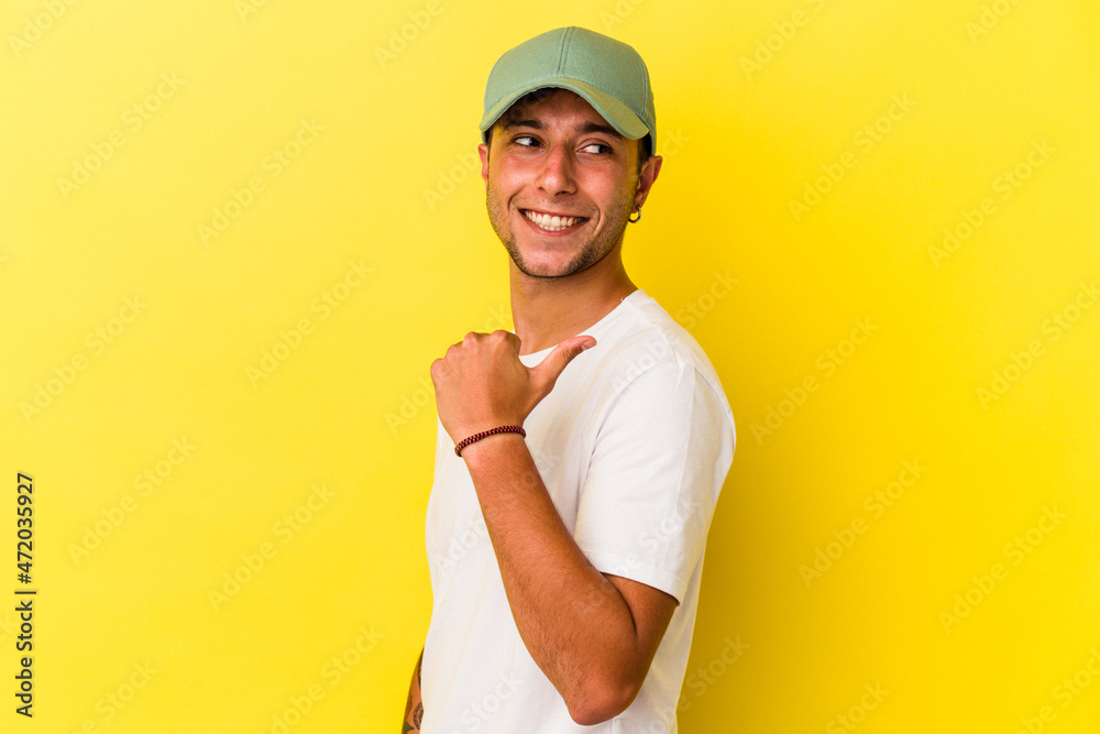 Young caucasian man with tattoos isolated on yellow background points with thumb finger away, laughing and carefree. Young caucasian man with tattoos isolated on yellow background points with thumb finger away, laughing and carefree.