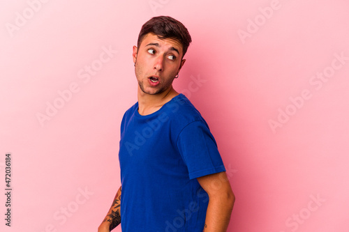 Young caucasian man with tattoos isolated on yellow background looks aside smiling, cheerful and pleasant.