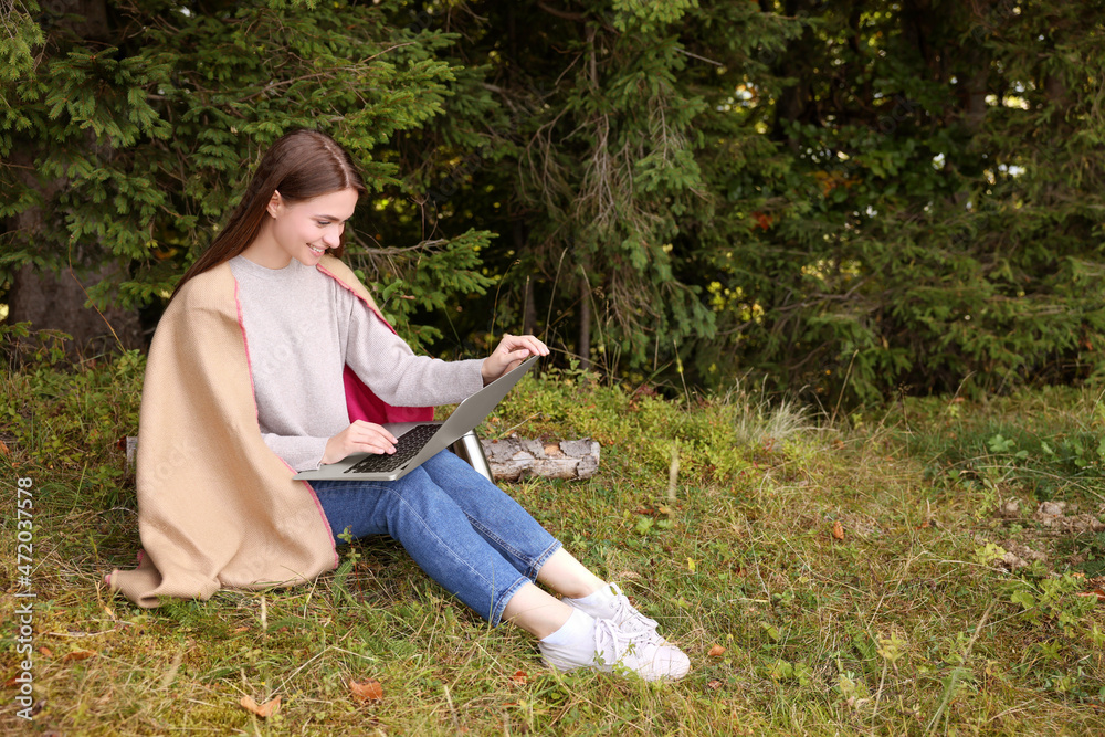Fototapeta premium Young woman working on laptop in forest, space for text