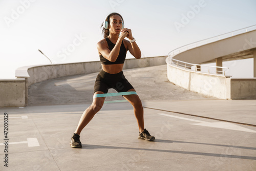 Black sportswoman working out with expander stretch tape on parking