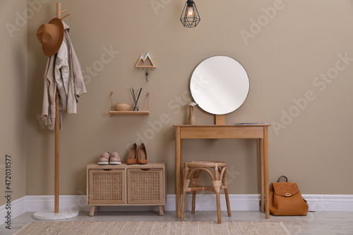 Modern hallway interior with stylish furniture, round mirror and wooden hanger for keys on beige wall © New Africa