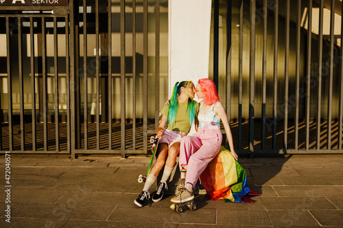Young lesbian couple kissing while sitting with rainbow flag