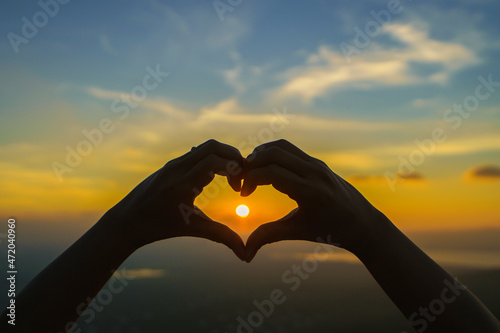 Woman hands silhouette on beautiful sunset above the mountain in the form of love heart-shaped hand gesture Concept of love  life  romance