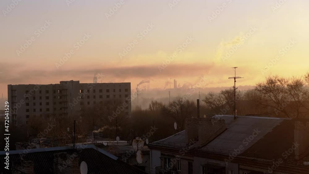 Gloomy View from the Window on Roofs of Old Houses of Smoky Industrial City. Working plants, factories, smoke from the chimneys of a thermal power plant in morning at sunrise. Ecological catastrophe. Gloomy View from the Window on Roofs of Old Houses of Smoky Industrial City. Working plants, factories, smoke from the chimneys of a thermal power plant in morning at sunrise. Ecological catastrophe.