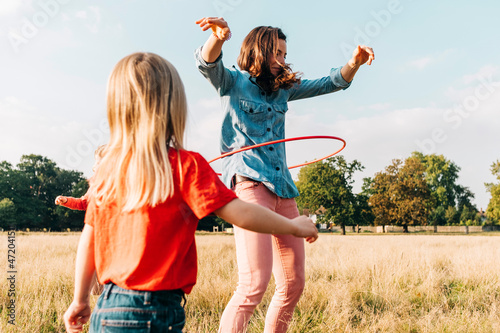 Mother spinning hula hoop by daughter in park