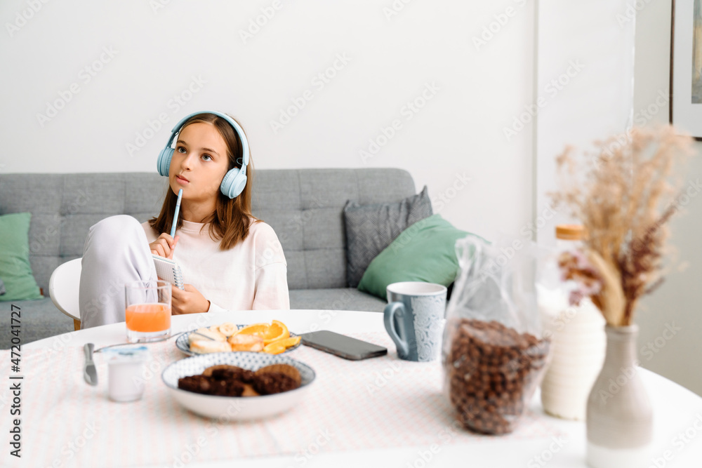 White girl in headphones doing homework while having breakfast
