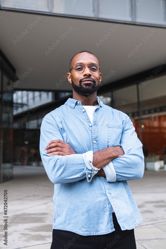 Man in casual clothing standing with arms crossed near buildings Man in casual clothing standing with arms crossed near buildings
