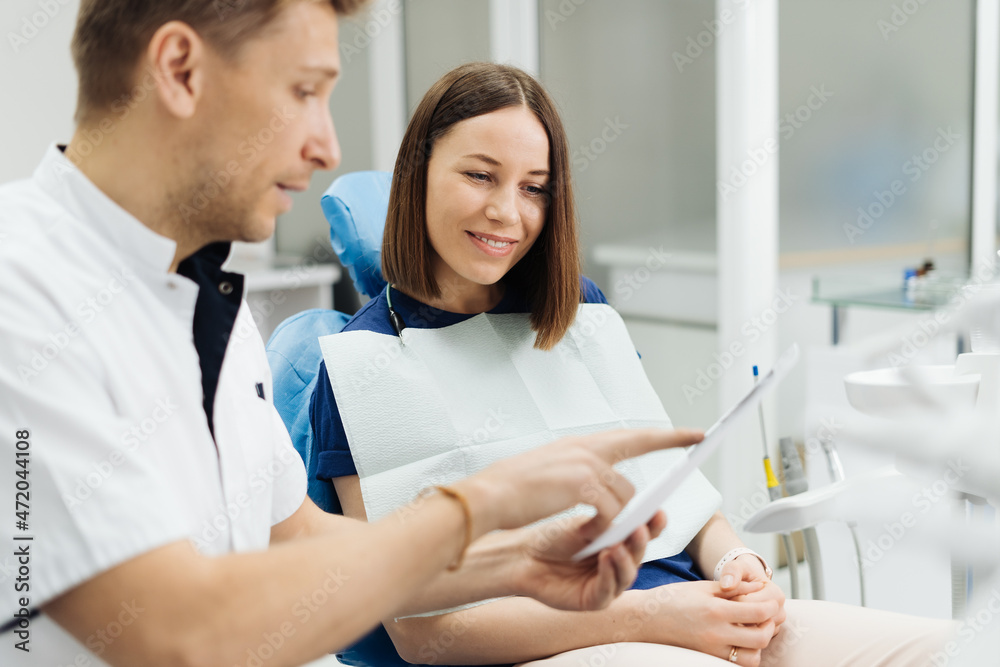 Fototapeta premium Male Professional Dentist With Gloves And Mask Holding papers photo And Show What The Treatment Will Look Like Of The Patient's Teeth. Discussion Of The Treatment Plan And Healthy Smile