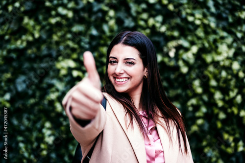 Smiling businesswoman showing thumbs up in front of ivy plants photo