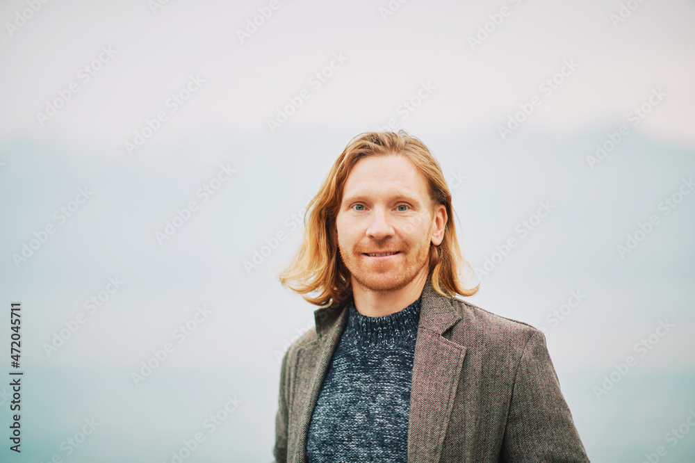 Outdoor portrait of happy young red haired man, wearing pullover and coat, cold foggy day Outdoor portrait of happy young red haired man, wearing pullover and coat, cold foggy day