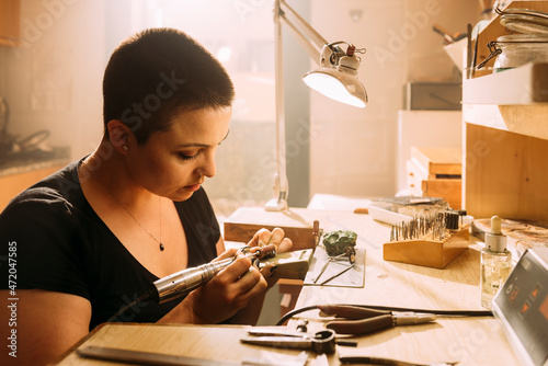 Female jeweler making silver ring using work tool in workshop photo