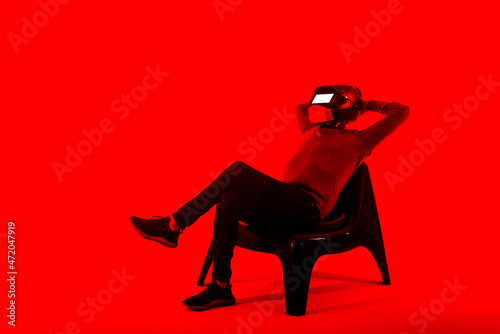 Relaxed man wearing futuristic helmet sitting on chair against red background