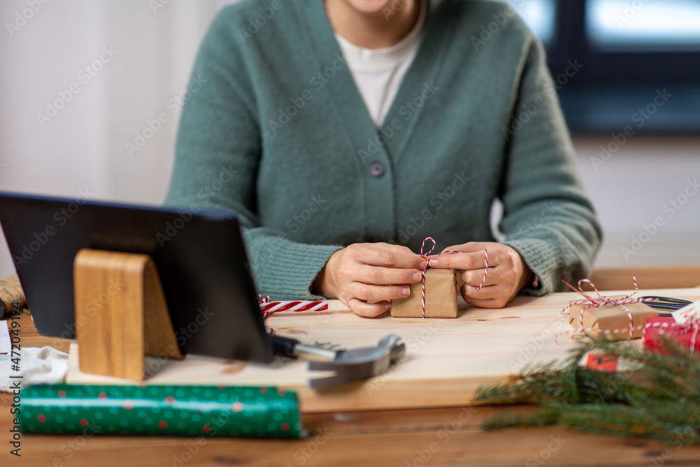 winter holidays and hobby concept - close up of woman with tablet pc computer packing christmas gift or making advent calendar at home