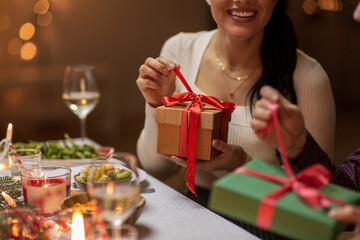 winter holidays and celebration concept - close up of happy smiling people opening christmas gifts at home dinner party