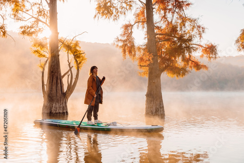 Woman on paddle board at lake with morning fog and autumnal Taxodium distichum photo