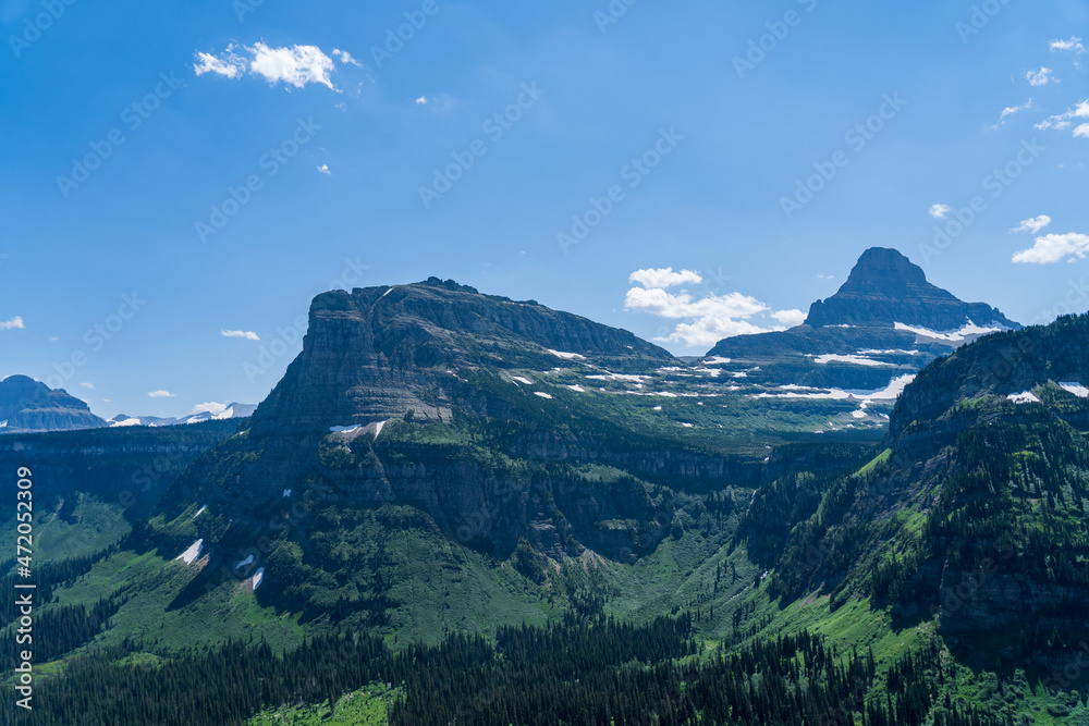 Naklejka premium View from Logan Pass in Glacier National Park, Montana on a sunny summer day, with glacial valley, snow-capped mountains, alpine lakes, and grass