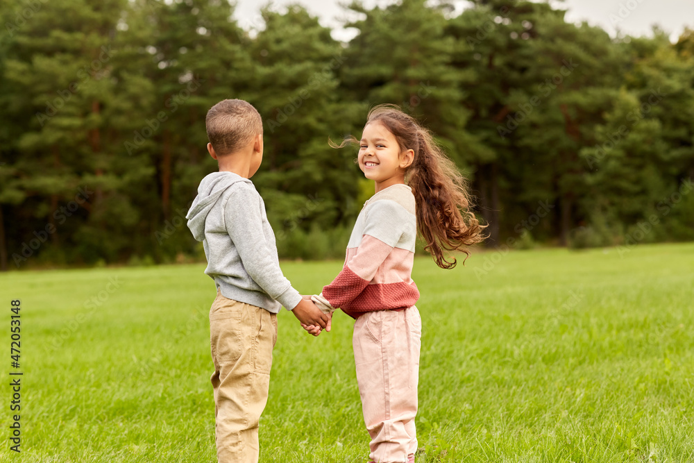 childhood, leisure and people concept - happy smiling little boy and girl holding hands at park childhood, leisure and people concept - happy smiling little boy and girl holding hands at park