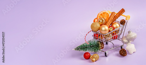 A cart with Christmas decorations on a purple background. The concept of buying gifts for the new year and Christmas