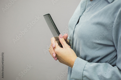 Comb in the hands of a girl on a gray background. Hair care. New hairstyle. photo