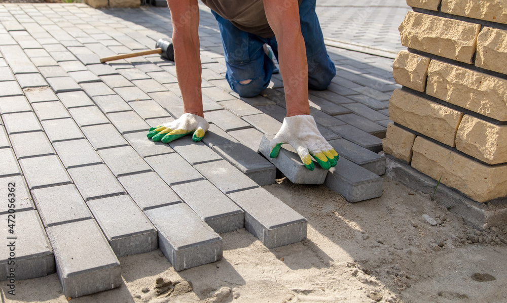 A worker is laying paving slabs in the yard. Construction A worker is laying paving slabs in the yard. Construction