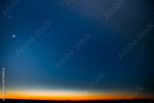 Night Starry Sky With Glowing Stars Above Countryside Field Landscape In Early Spring. Bright Glow Of Planet Venus In Sky Among The Stars. Sky In Warm Lights Of Evening Sunset Dawn Or Morning Sunrise
