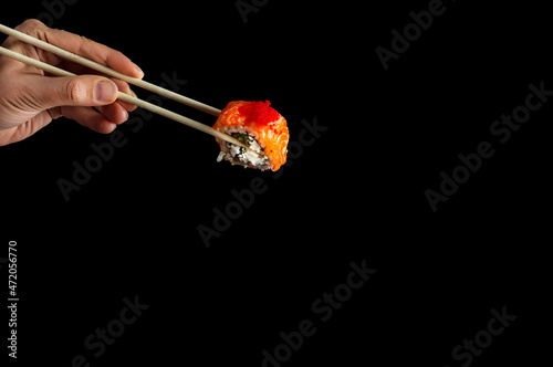 japanese sushi food. Women's hands hold sushi rolls with sticks. Isolated on black. Popular food concept..